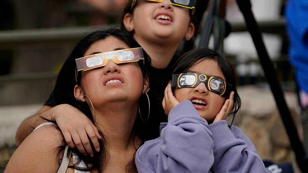 Person holding ISO-certified solar eclipse safety glasses up to bright sunny sky in Spain