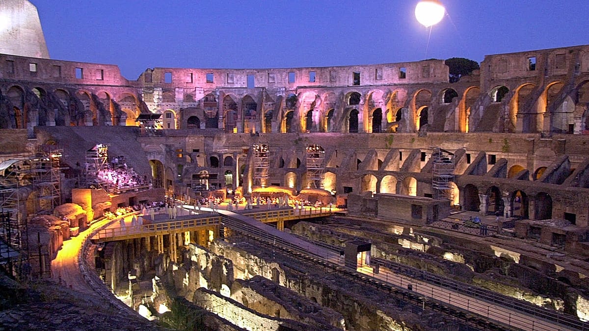 The ancient Roman Colosseum illuminated against a twilight sky with evening visitors