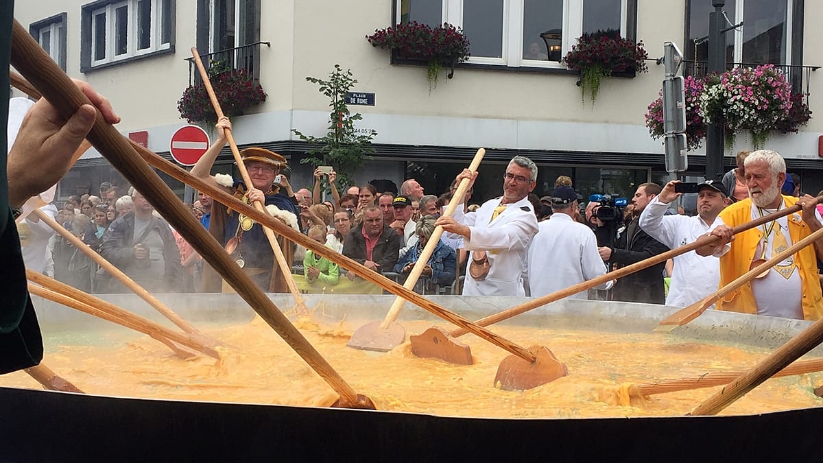 Volunteers stirring giant omelette in massive four-meter pan over open fire at Belgian festival