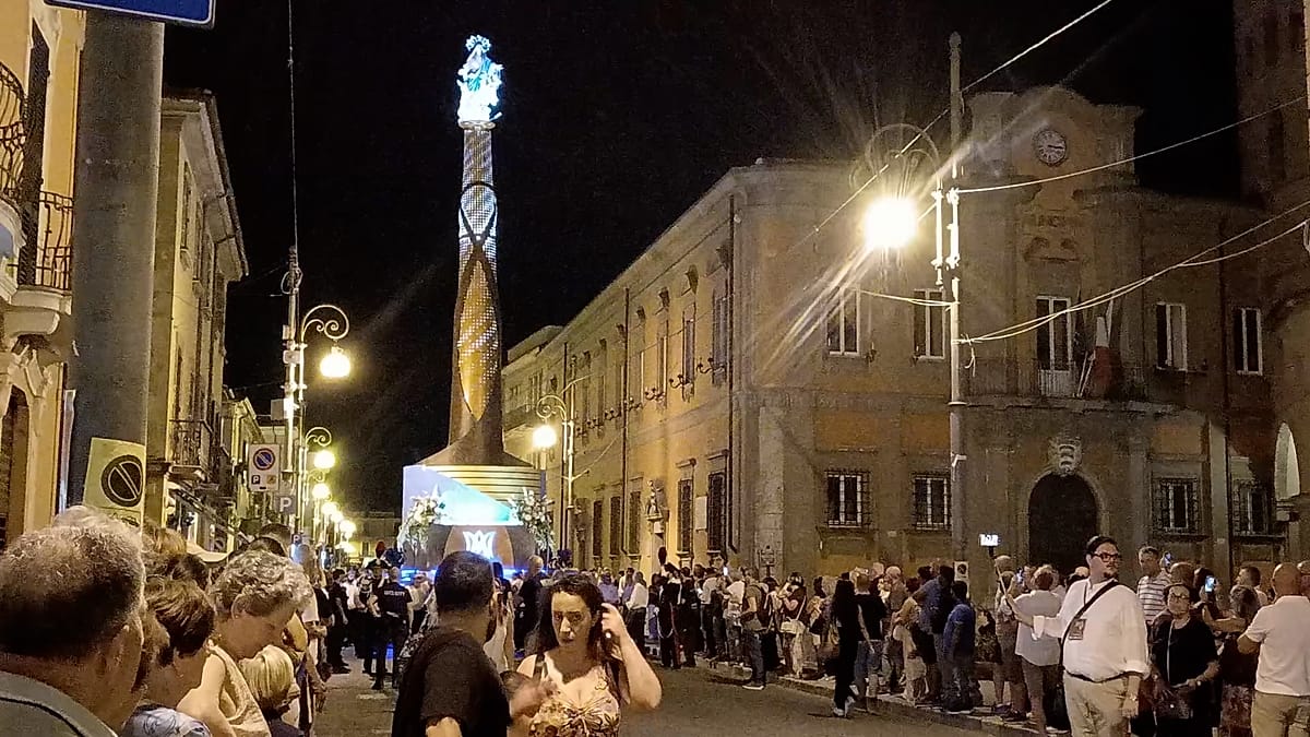 Towering illuminated religious structure carried through Italian streets at night surrounded by celebrating crowds