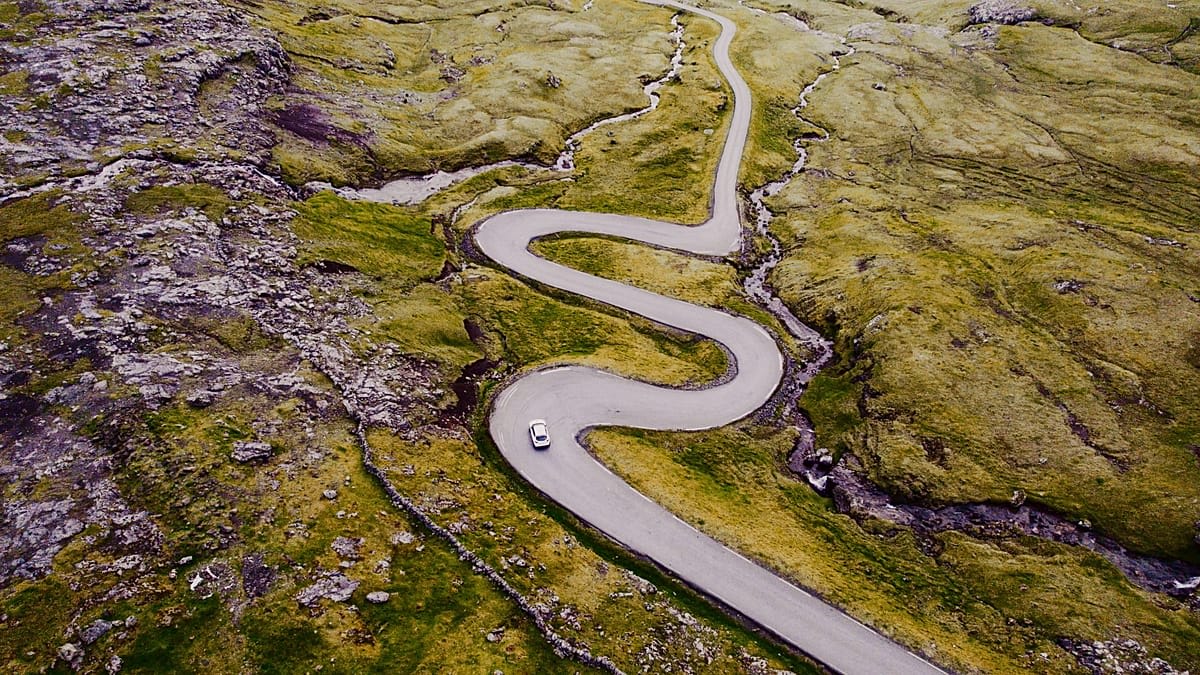 Winding coastal road through dramatic green cliffs in the Faroe Islands under moody skies