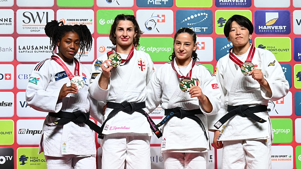 Judo athletes competing on mat at Lausanne Grand Slam tournament with Olympic officials watching