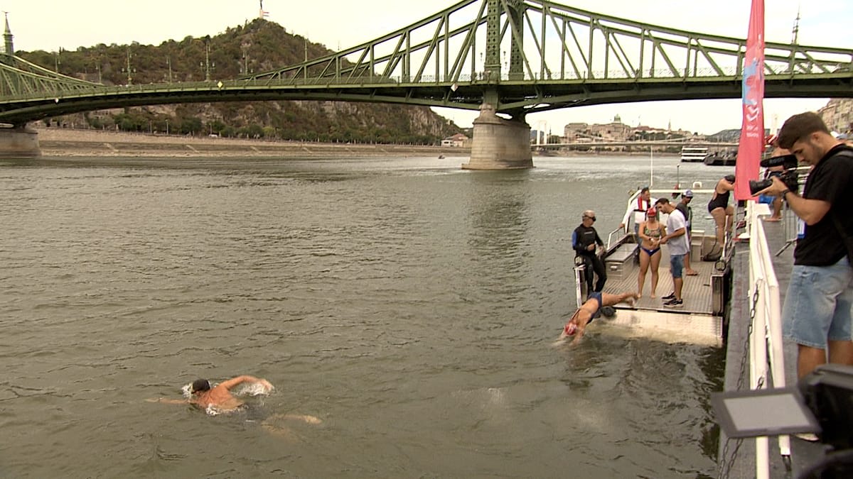 Hundreds of swimmers crossing the Danube River in Budapest with historic cityscape behind them