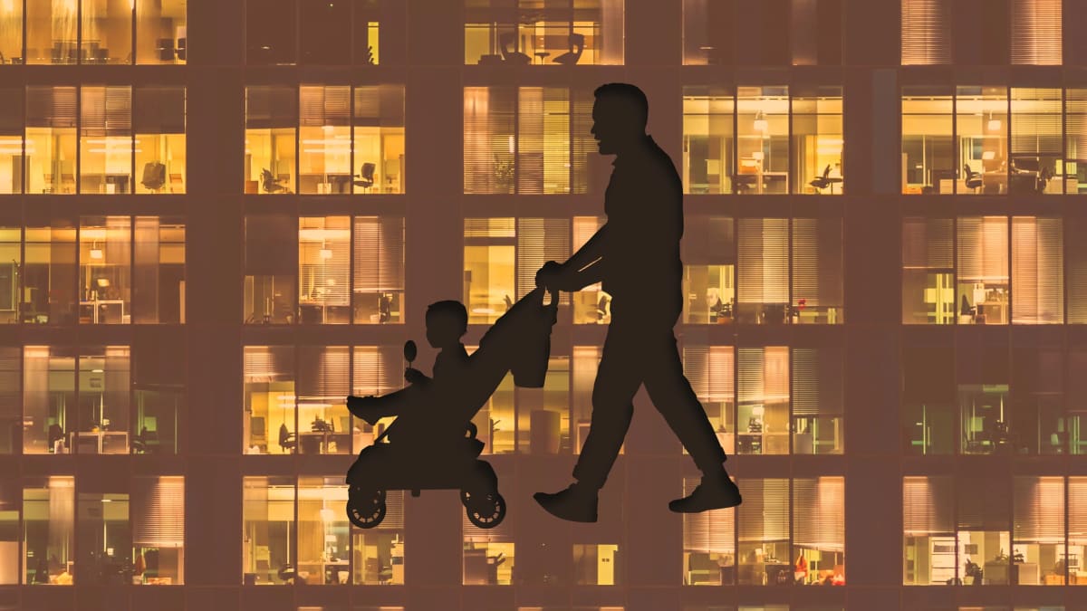 Father holding newborn baby while working on laptop at home office desk