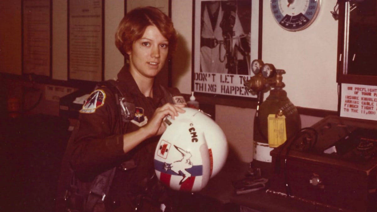 Astronaut Eileen Collins in orange flight suit standing confidently before space shuttle launch