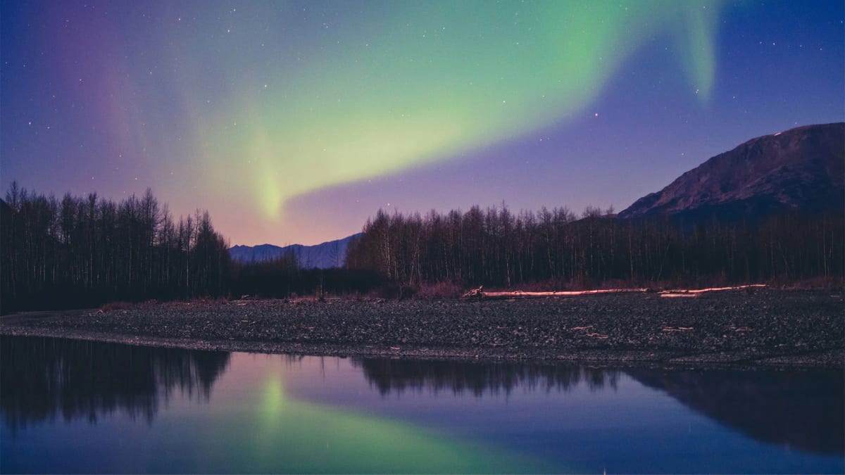 Green and purple northern lights dancing across a dark night sky over northern landscape