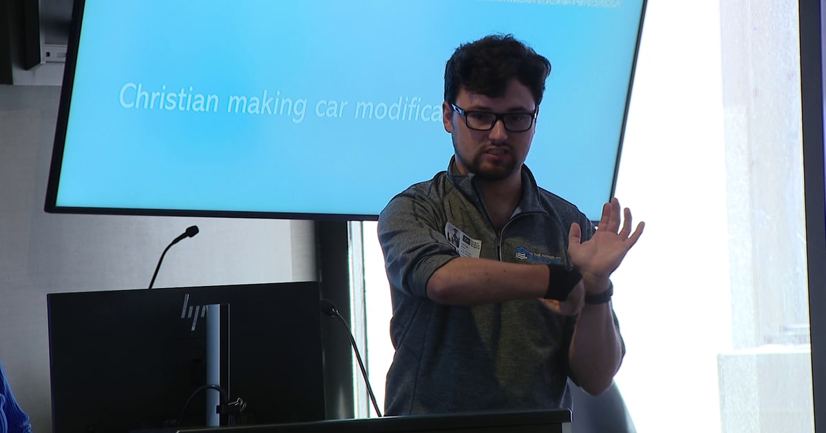 Young man demonstrating arm movement with chest-implanted Vivistim device at Tampa hospital event