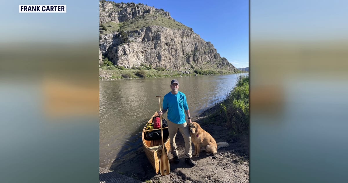 Frank Carter paddling handmade wooden canoe on river with his dog Amos