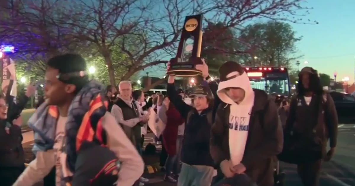 University of Mary Washington men's basketball team celebrating with NCAA championship trophy surrounded by cheering fans