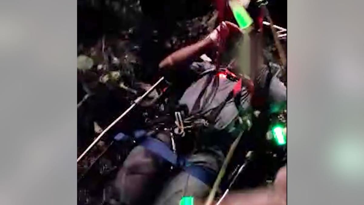 Black Hawk helicopter conducting nighttime mountain rescue operation with hoist deployment over rugged terrain