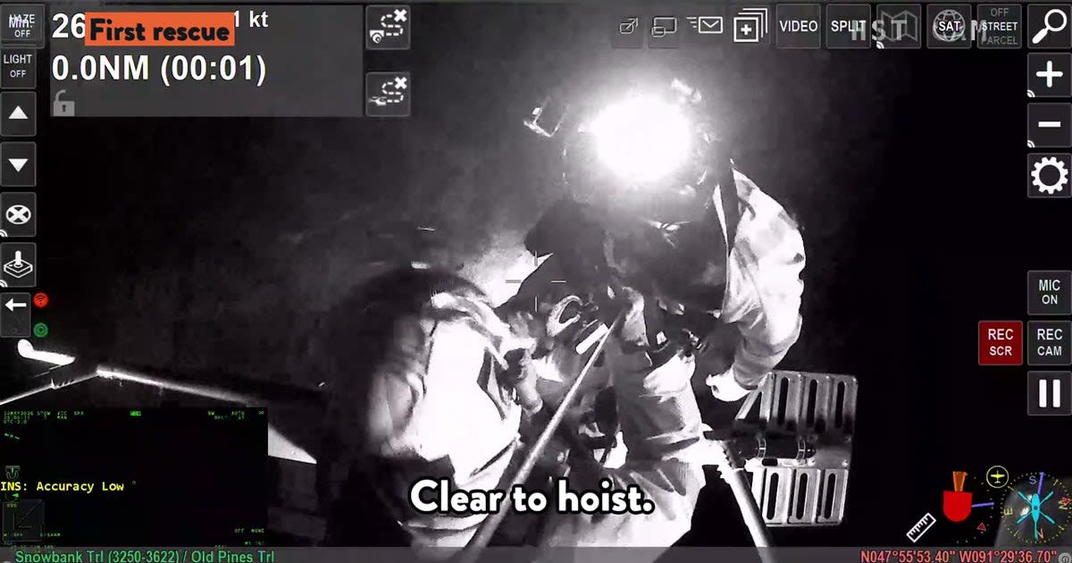 Helicopter rescue team lowering rescuer between trees at night to reach stranded canoers