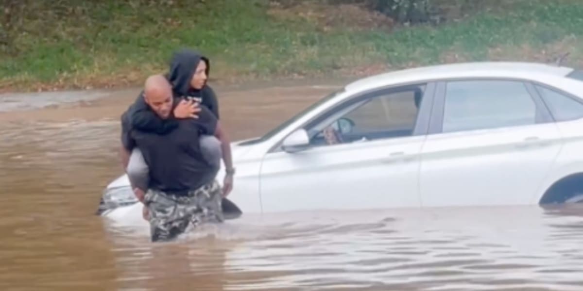 Man carrying woman on his back through waist-deep floodwater on Atlanta highway
