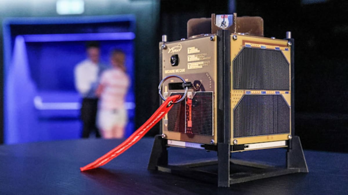 Small cube-shaped satellite with extended solar panels floating in space orbit above Earth