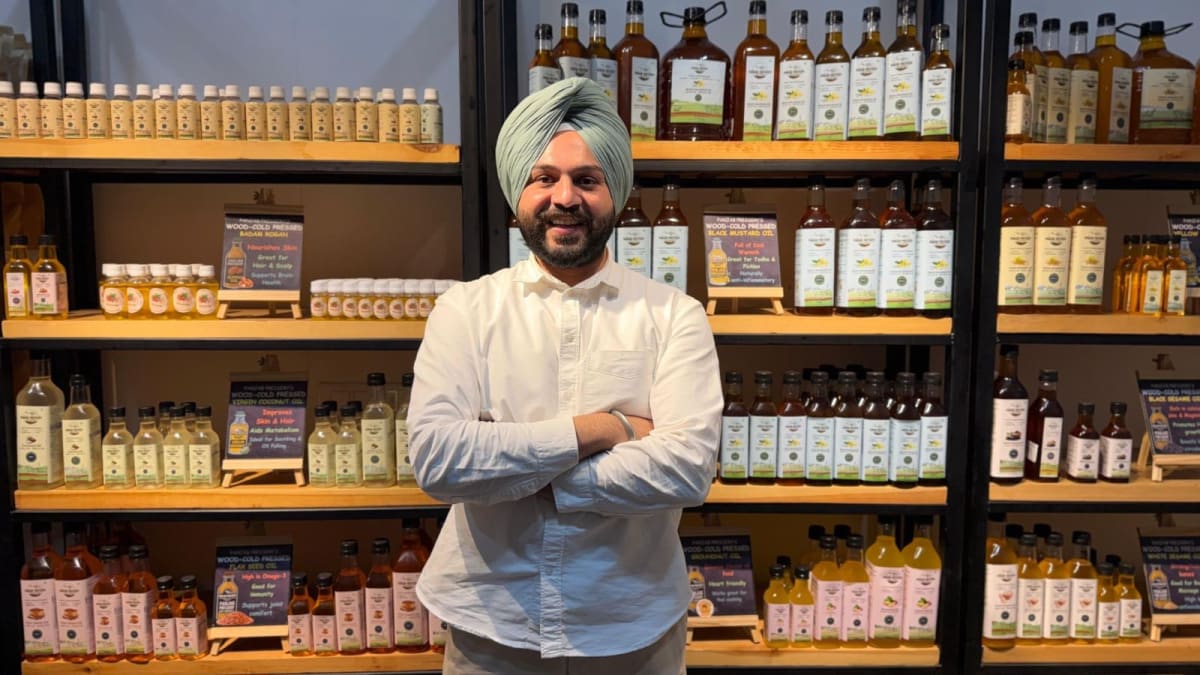 Young Indian farmer standing beside traditional wood-press oil extraction machines in clean, glass-walled facility