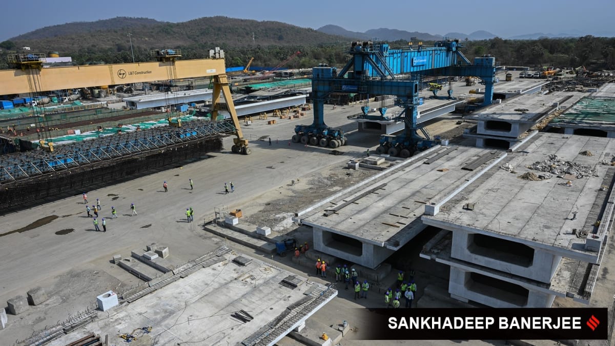 Massive blue straddle carrier lifting concrete girder at India's bullet train construction site in rural Maharashtra