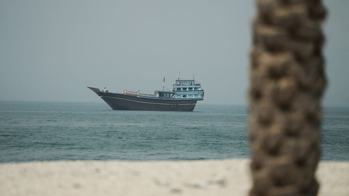** Cargo vessel sailing through Strait of Hormuz waters near Oman coast at dawn