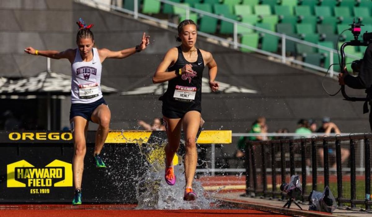 Female college track athlete competing in steeplechase event clearing water barrier at stadium