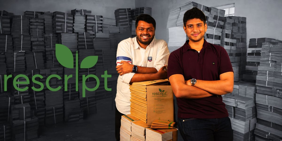 Two young Indian entrepreneurs standing with stacks of recycled paper notebooks in Bengaluru office