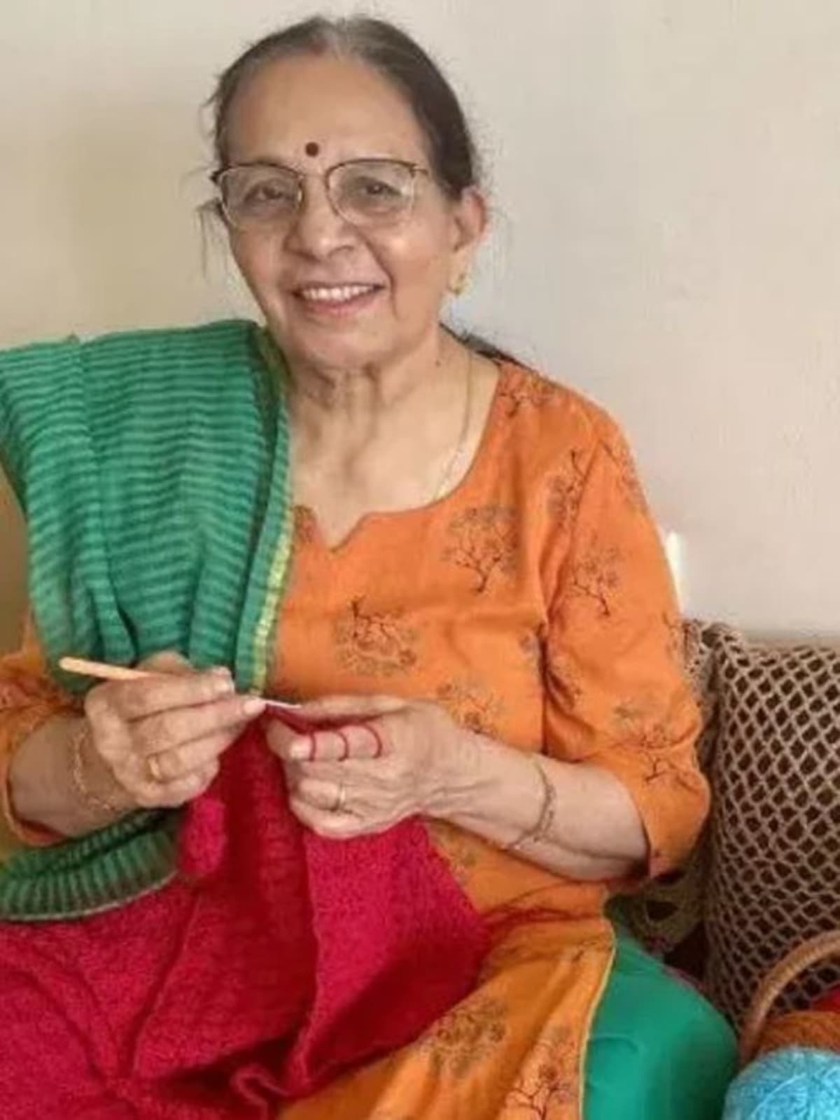 Elderly Indian woman in Mumbai holding colorful handmade crochet jacket with intricate patterns