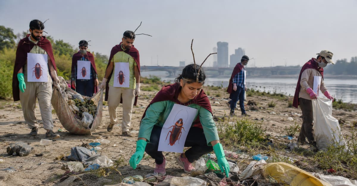 Volunteers in cockroach costumes cleaning plastic waste along polluted Yamuna River banks in Delhi