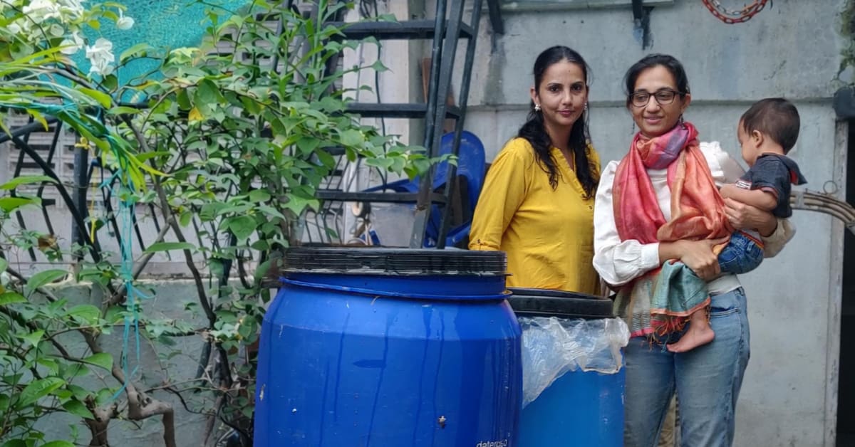 Two women checking large fermentation drums filled with lemon peels on Mumbai terrace