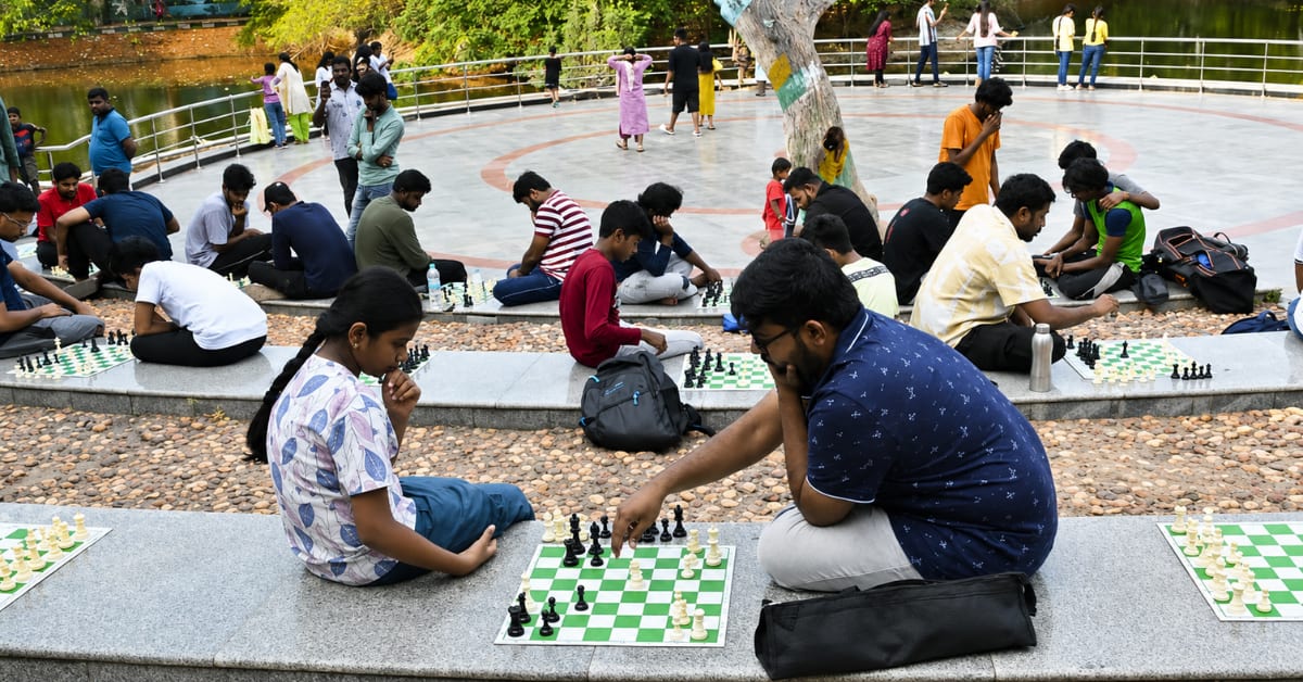 Chess players of various ages gather around boards in Chennai park under trees