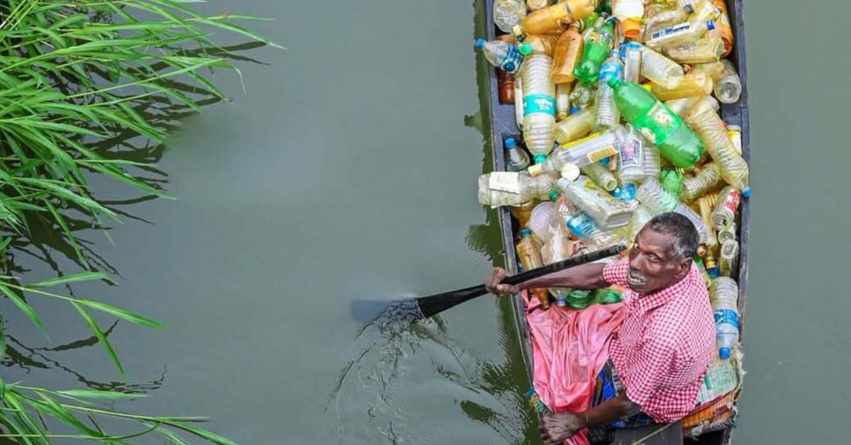 Elderly man in wooden boat surrounded by collected plastic bottles on Kerala river