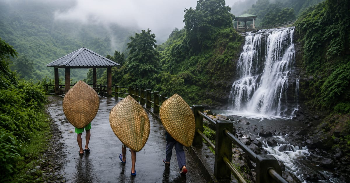 Villager wearing curved bamboo and banana leaf knup rain shield in misty Mawsynram, India