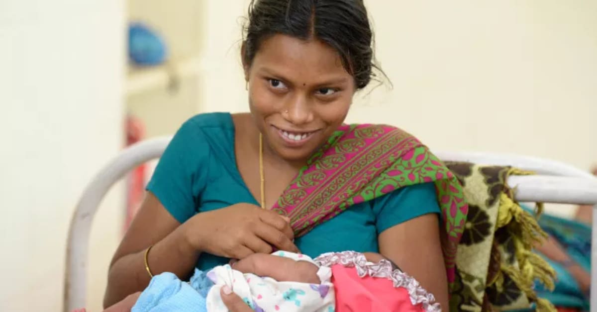 Mother breastfeeding her infant baby while receiving support from healthcare professional in India