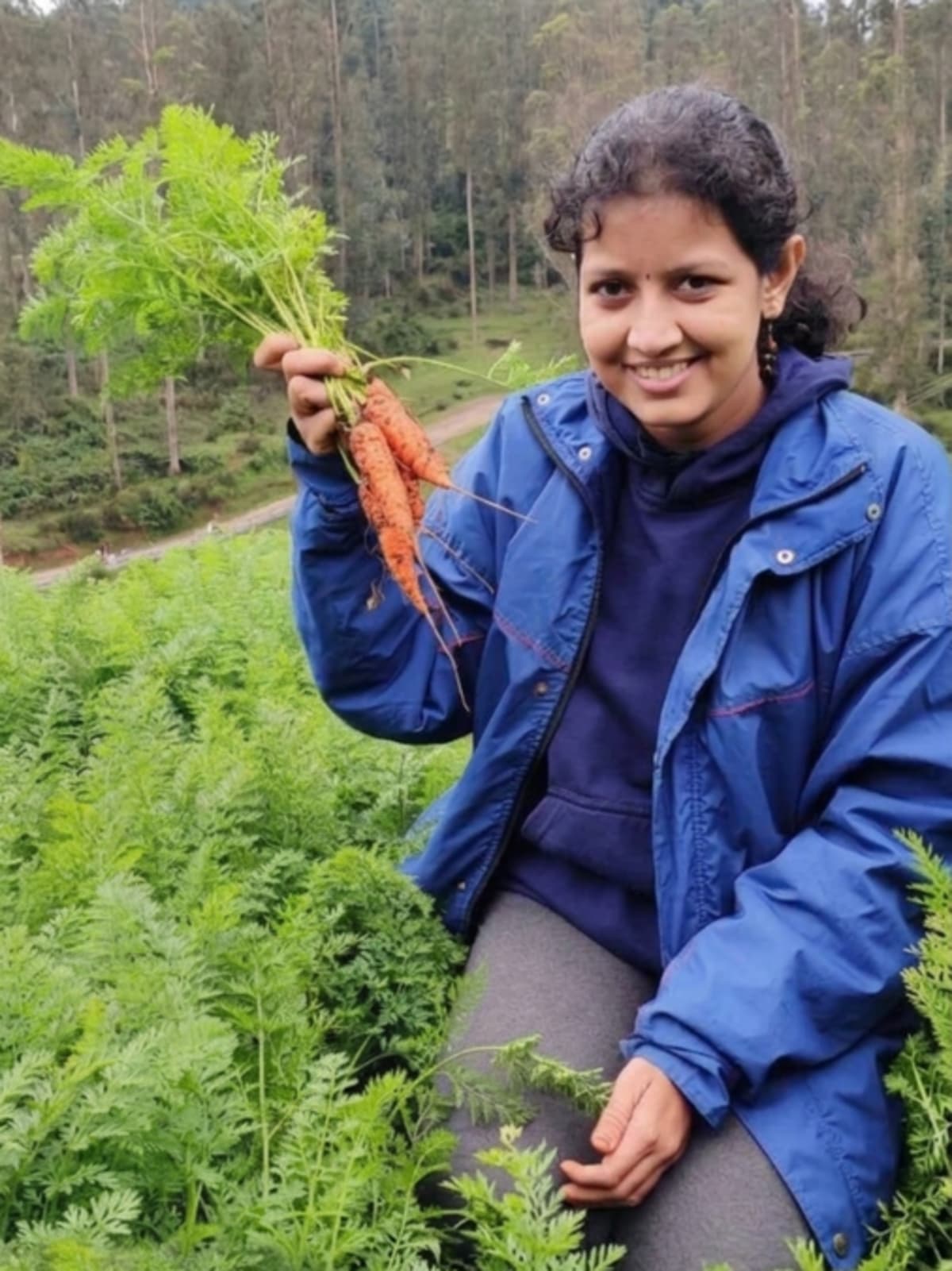 Archana Stalin standing in green farmland with fresh vegetables from myHarvest Farms platform