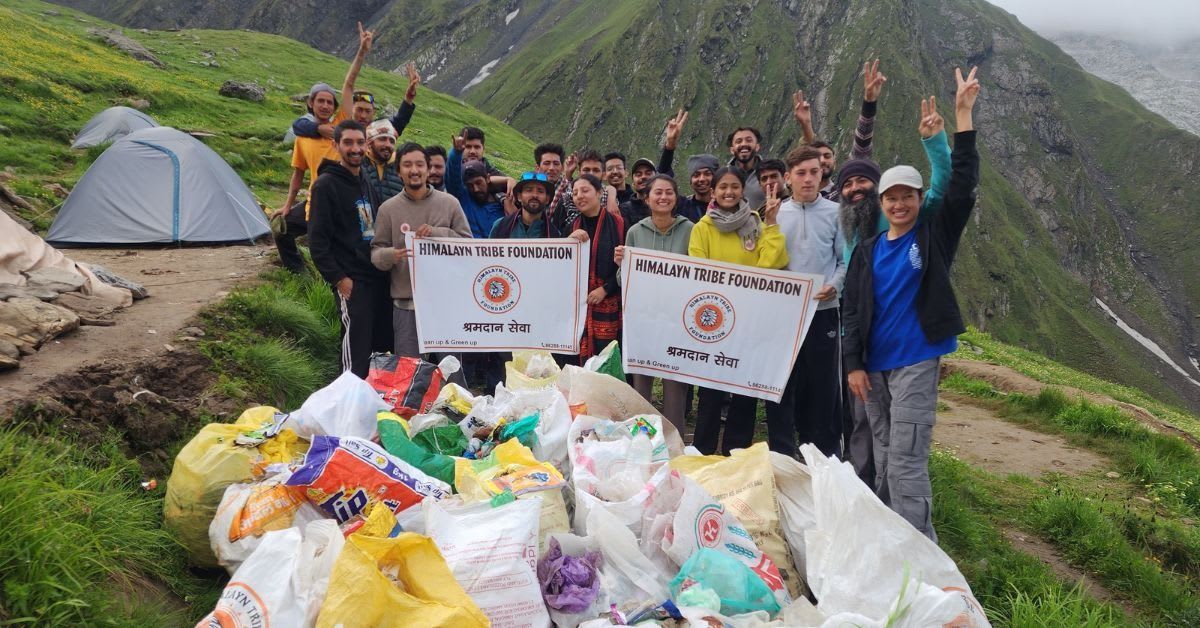 Volunteers carrying bags of collected waste down a snow-covered Himalayan mountain trail in India