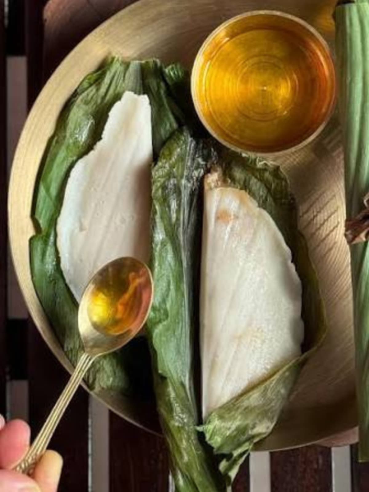 Steamed patoleo sweet wrapped in green turmeric leaves arranged on traditional plate