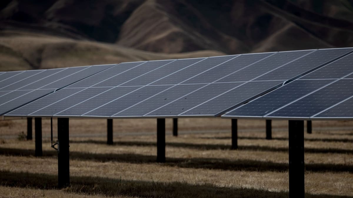 Large battery storage facility with solar panels stretching across landscape at sunset