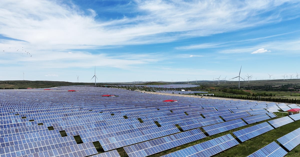 ** Modern solar panels and wind turbines with battery storage facility under bright blue sky