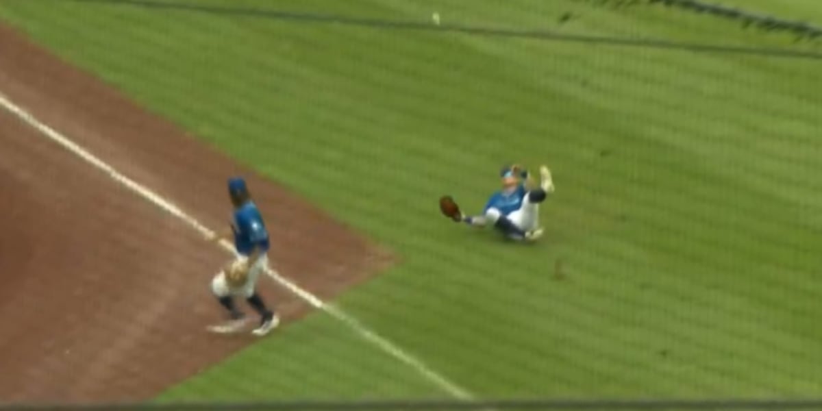 Baseball infielder making catch in shallow outfield while teammate slides nearby