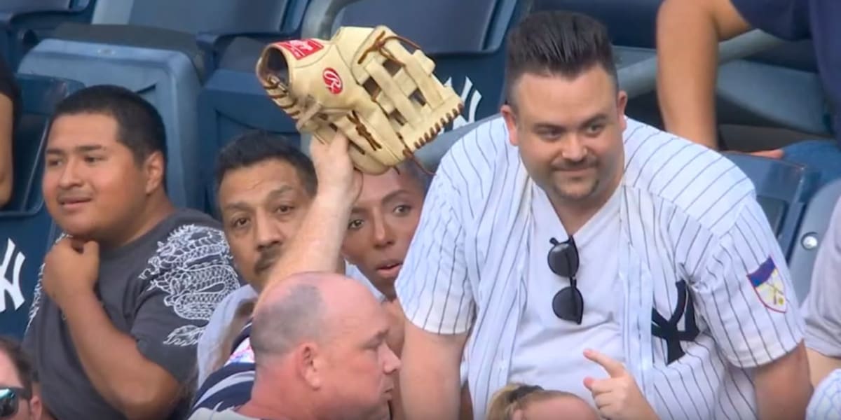 Baseball outfielder reaching up toward stadium wall with fans nearby in stands