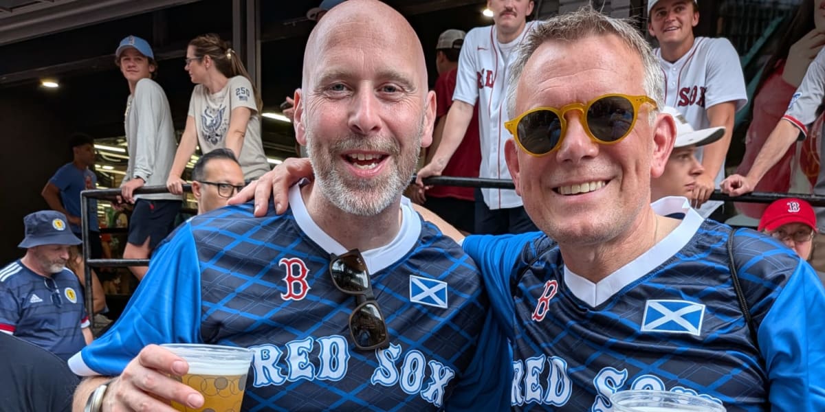 Scottish soccer fans in blue jerseys and kilts celebrating at Fenway Park's bleachers