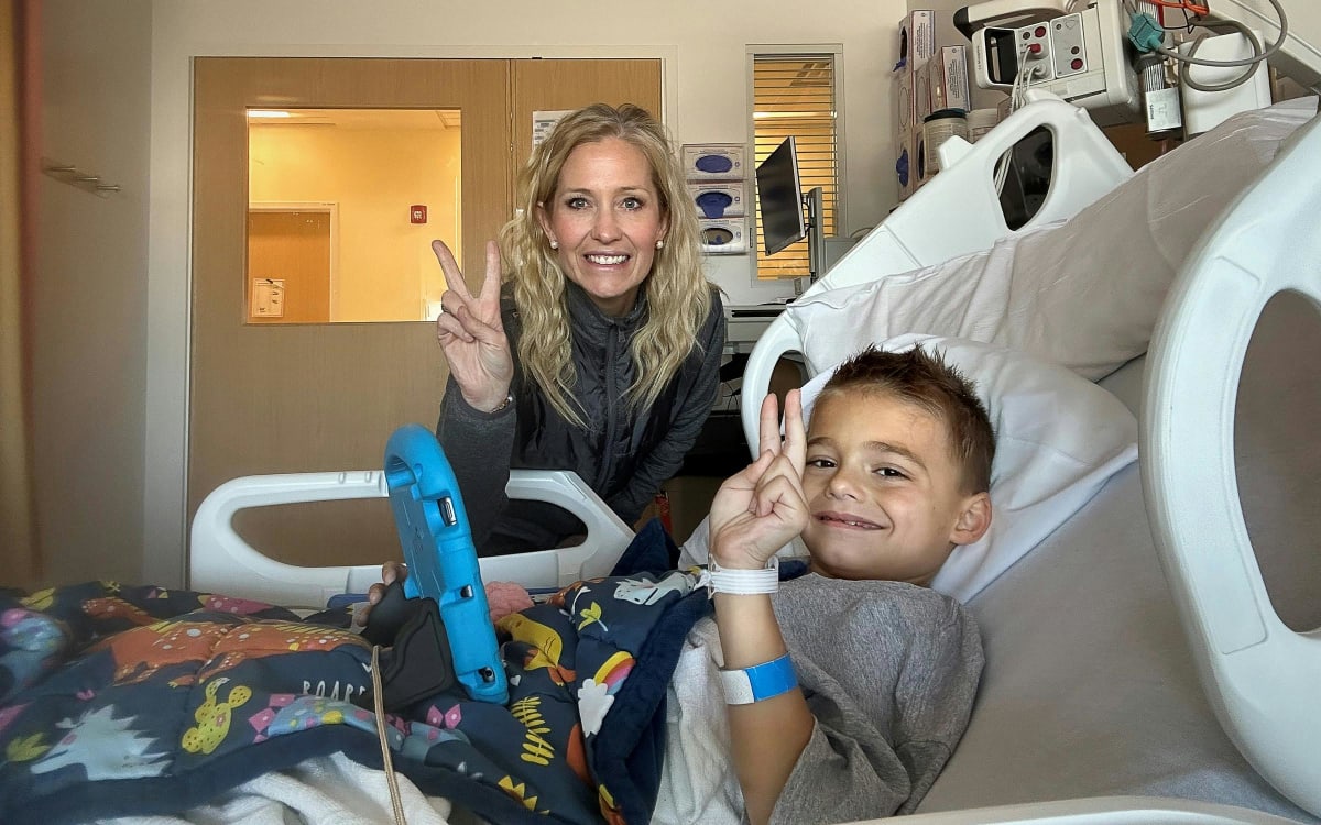Eight-year-old Maxwell Freed with sandy blond hair sits on his mother Amber's lap smiling
