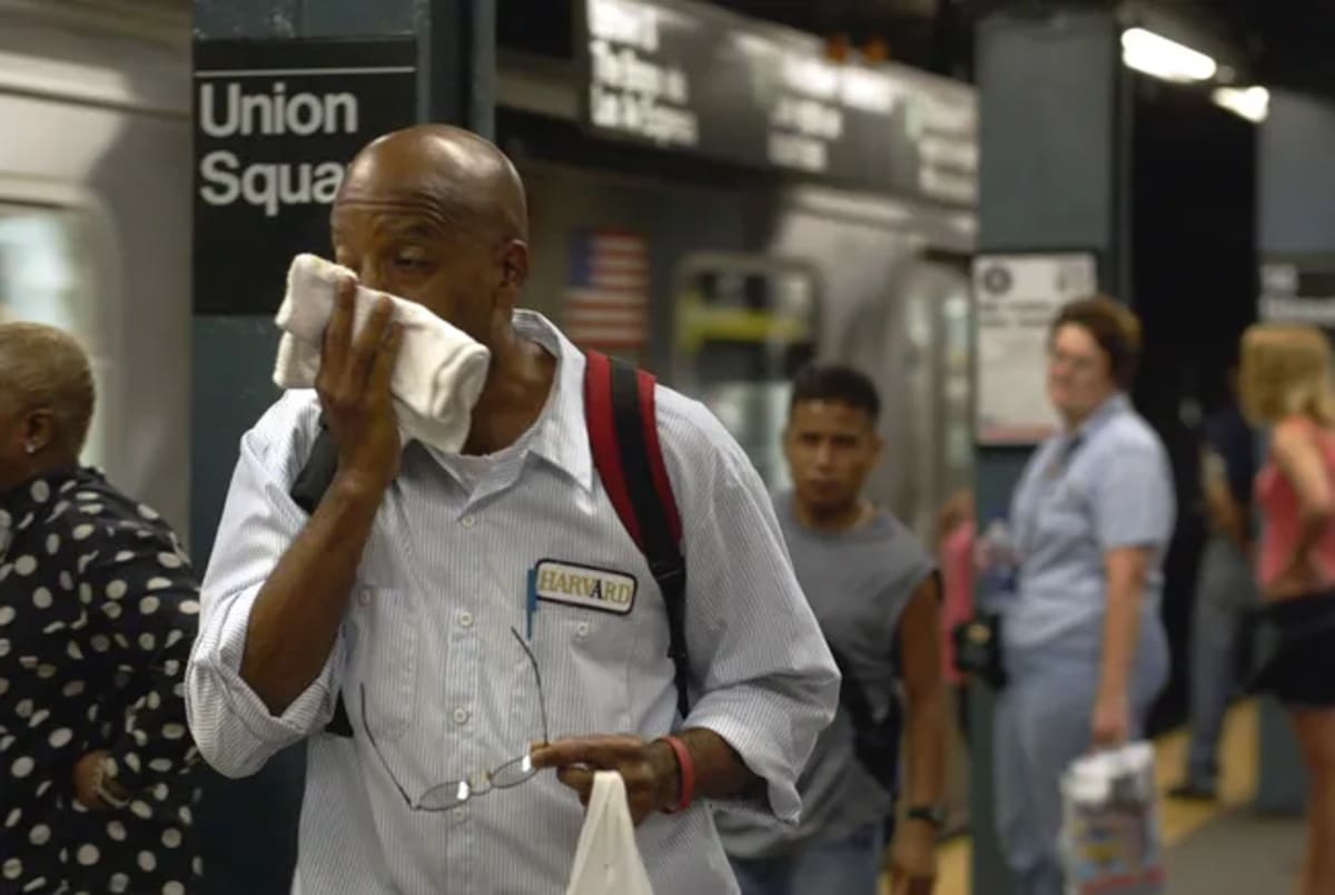 Commuters on hot New York City subway platform wiping sweat in summer heat