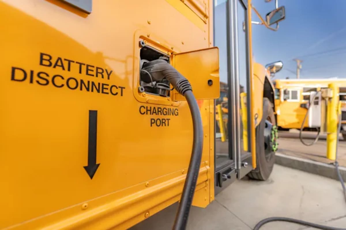 Yellow electric school bus plugged into charging station in Massachusetts parking lot