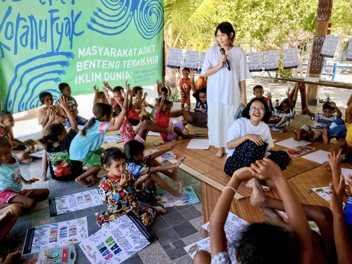 Children gathered on Arborek Island listening to a reading of an illustrated environmental storybook
