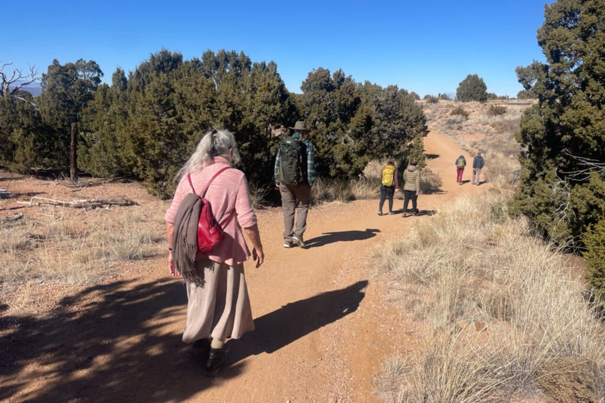 Three pilgrims walking along desert road with oil pump jacks visible in background