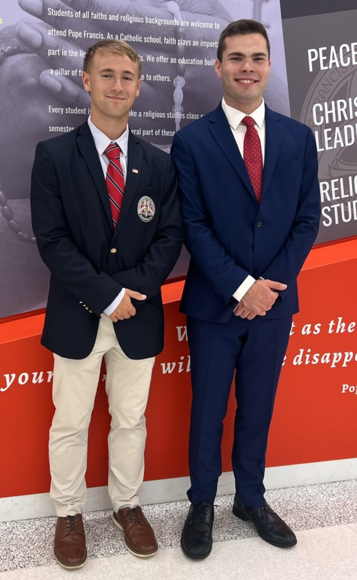 Two young men in formal attire pose together at school awards ceremony holding scholarship certificates