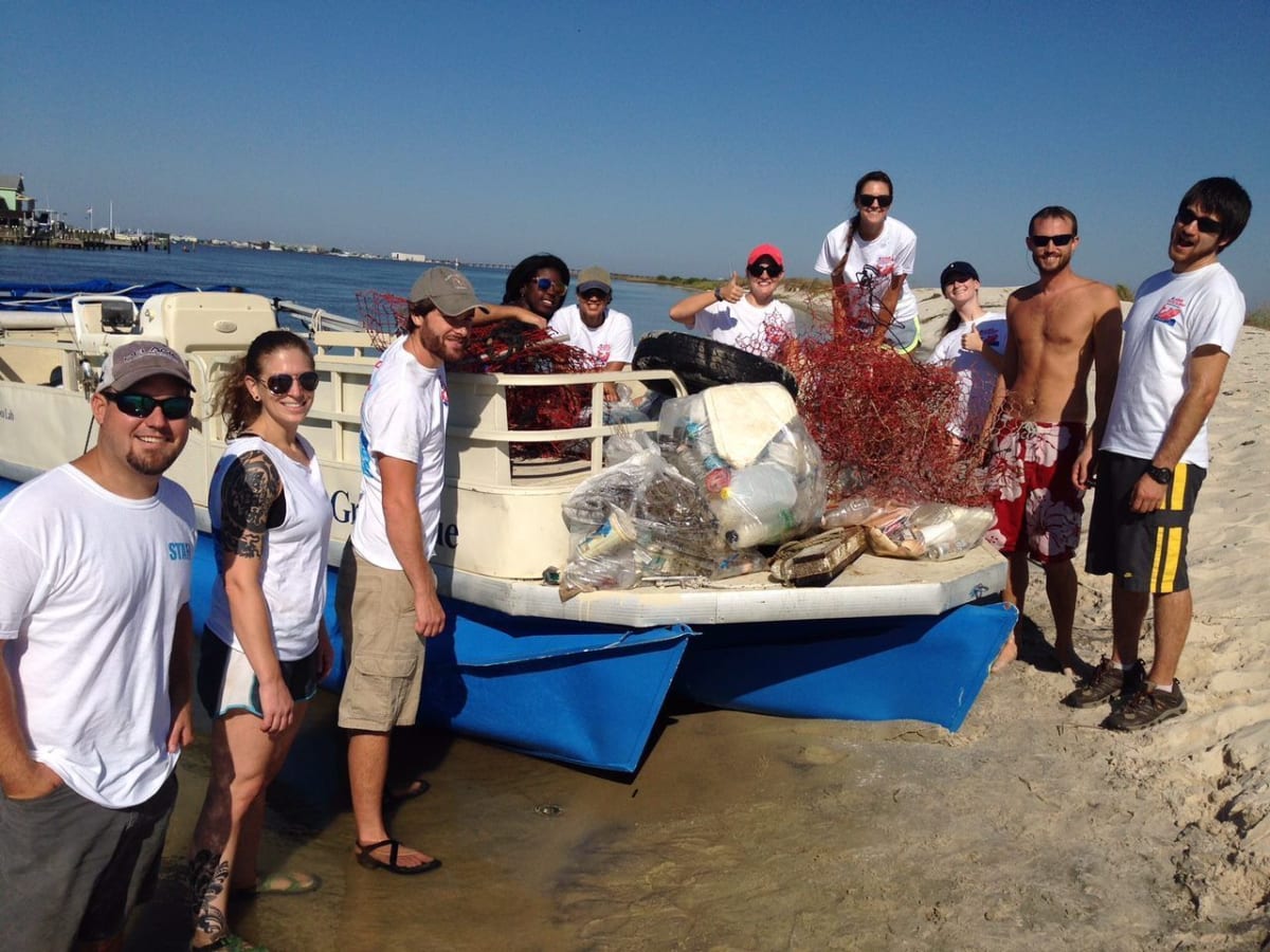 Volunteers collecting trash and debris along sandy Alabama coastline during annual beach cleanup event