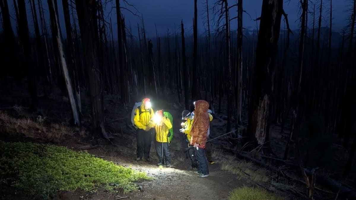 Search and rescue volunteers in winter gear help woman hiker back to trailhead after hypothermia rescue
