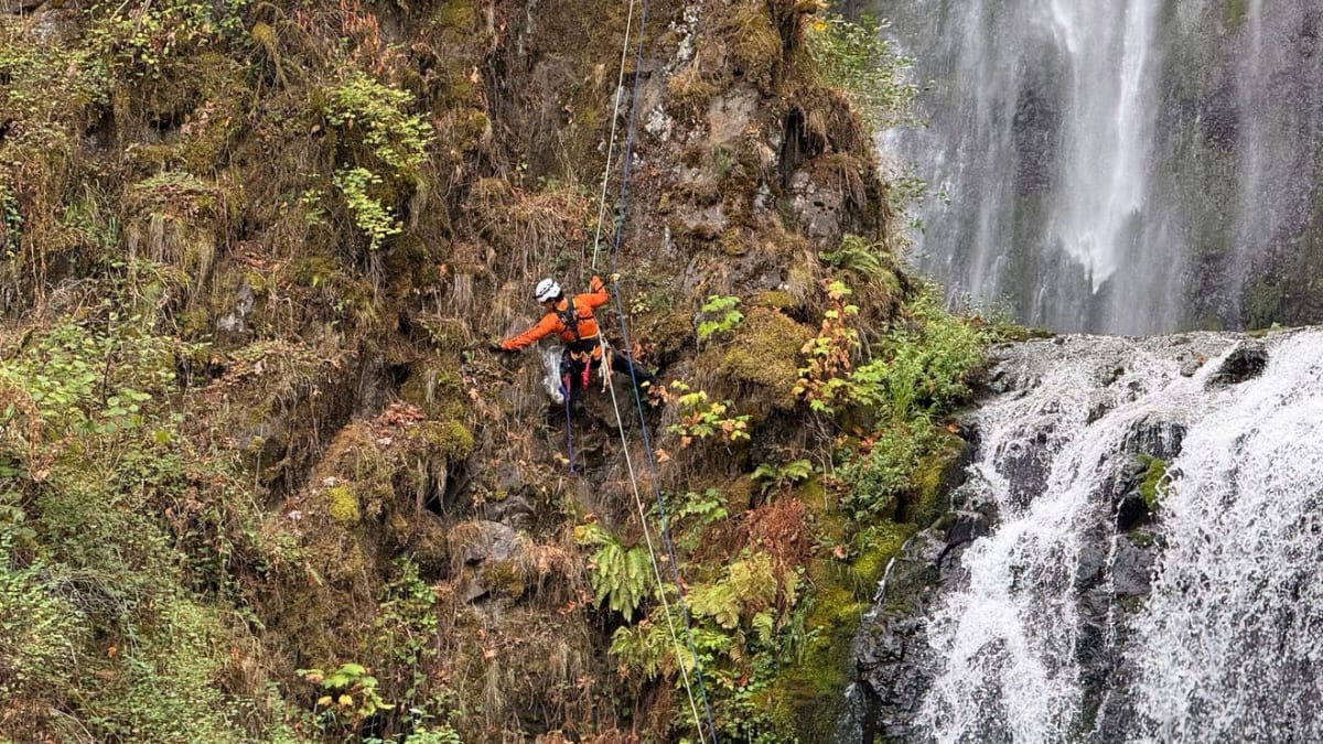 Search and rescue volunteer rappelling down Multnomah Falls waterfall while collecting litter during training exercise
