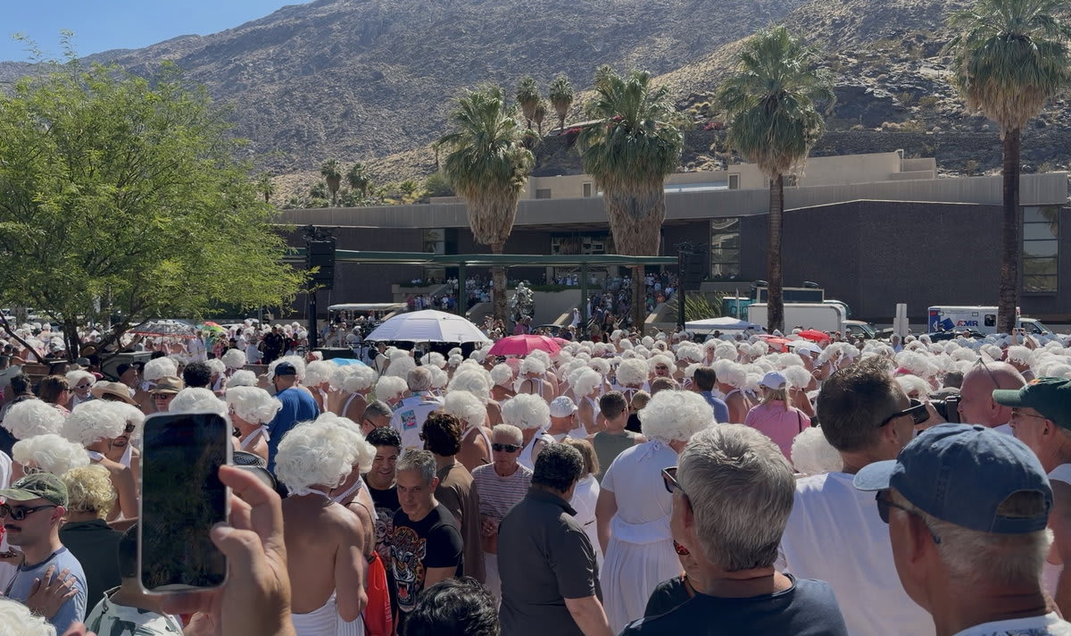 Large crowd dressed as Marilyn Monroe in white dresses and blonde wigs gathering in downtown Palm Springs