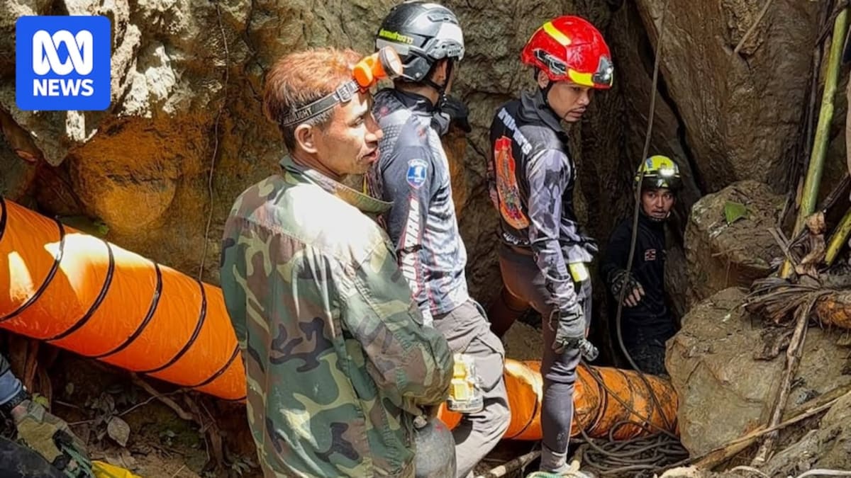 Rescue workers in helmets with headlamps navigate narrow muddy passage inside Laos cave