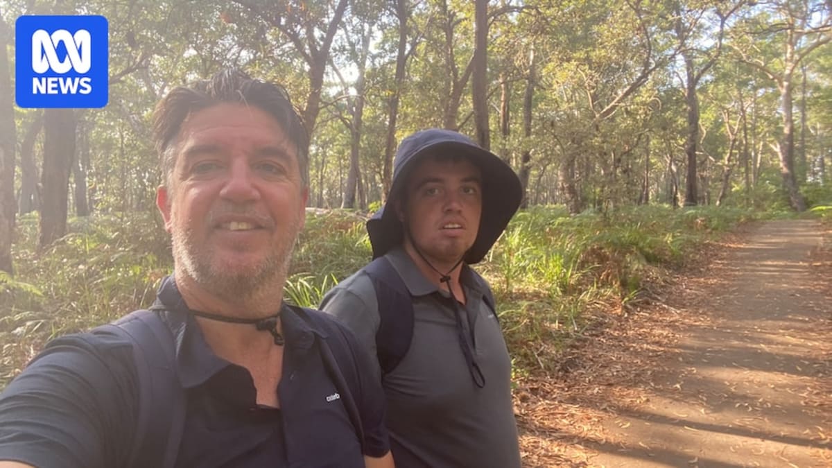 Father and teenage son hiking together through Australian bushland carrying backpacks