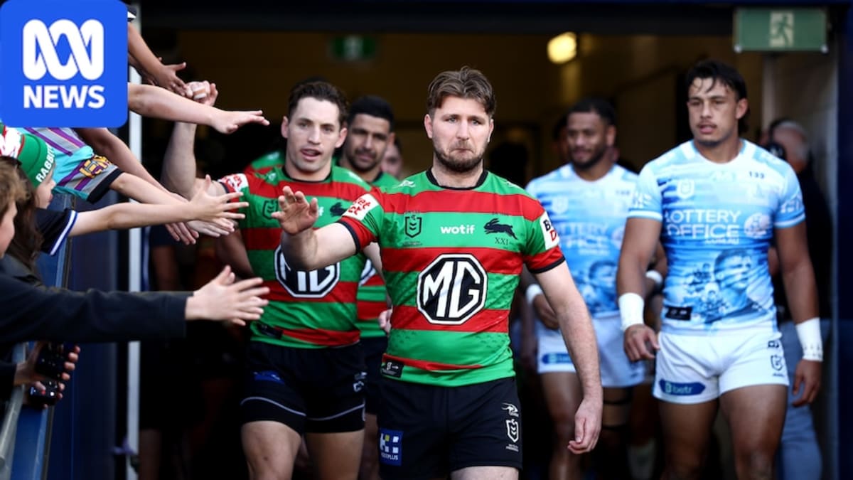 Jai Arrow in South Sydney Rabbitohs uniform being embraced by teammates on rugby field